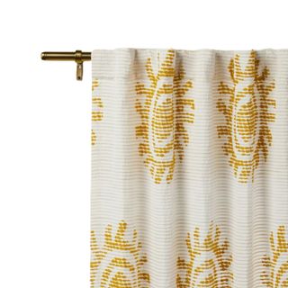 A white curtain panel with a yellow sun pattern on a metal rod