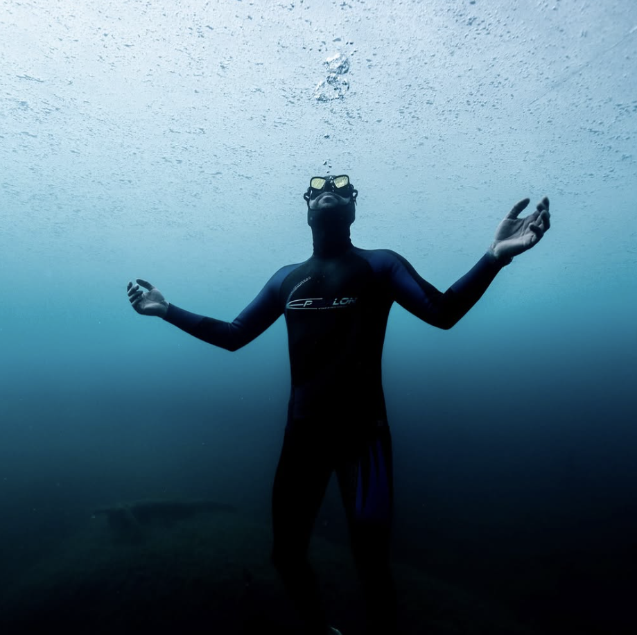 Man in a wetsuit and goggles holding his breath underwater