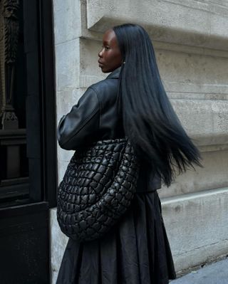 Woman wears leather jacket, black crossbody bag and black skirt