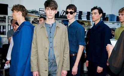 Male models wearing Margaret Howell S/S 2015 collection. Navy and denim is indicative of this collection and the model in front is wearing denim shirt, denim pants and a light brown overcoat with buttons