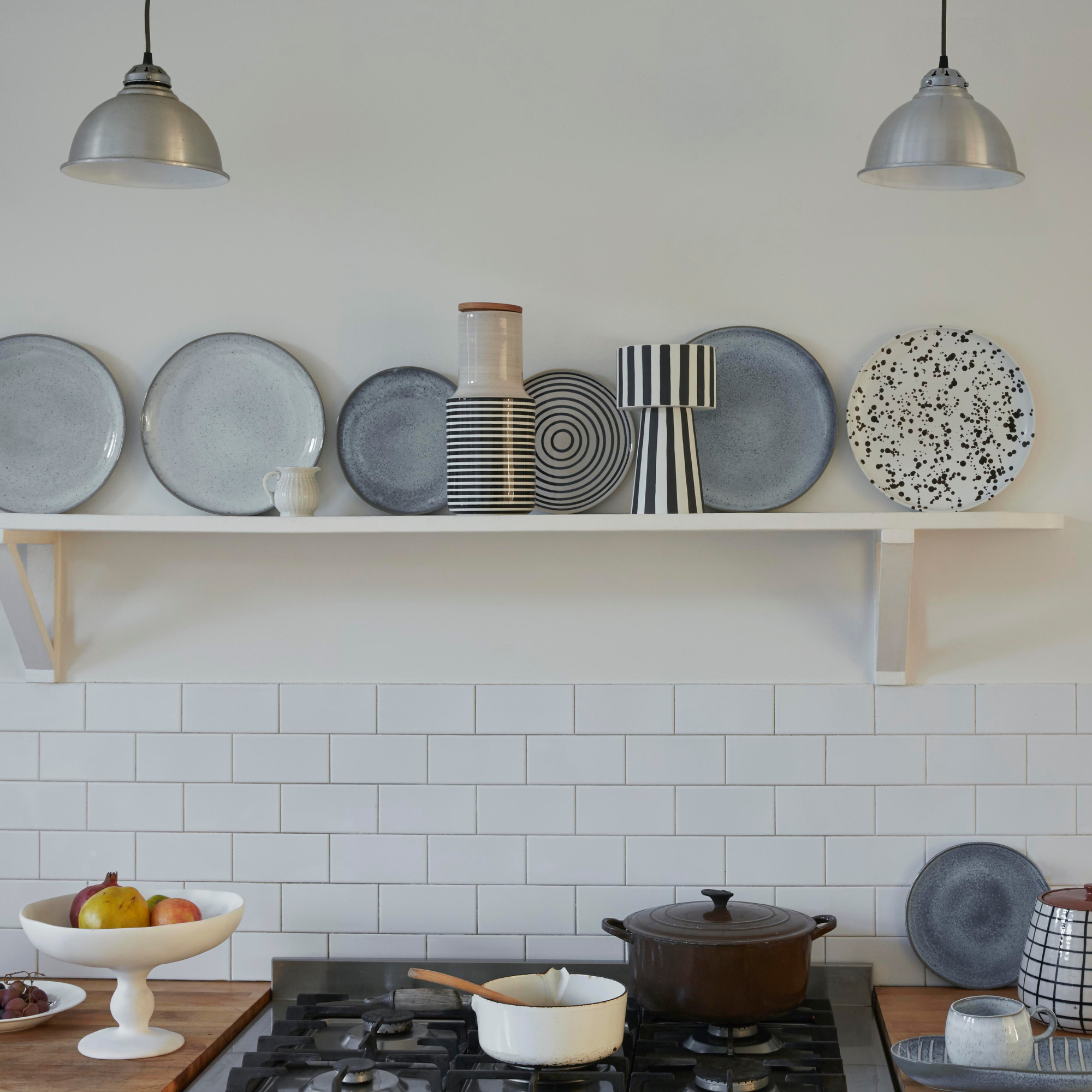 a white painted kitchen with white tiles and white shelf with plates displayed