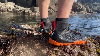 person wearing Vivobarefoot tempest water shoes on a rock near the sea