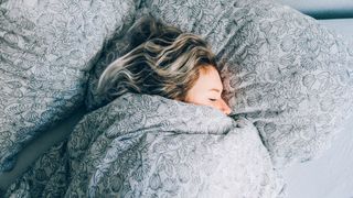 Woman snuggled up in a duvet in bed