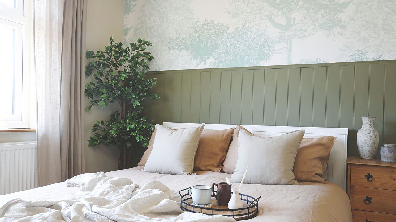 Neutral bedroom with sage green panelling behind the bed and tree wallpaper