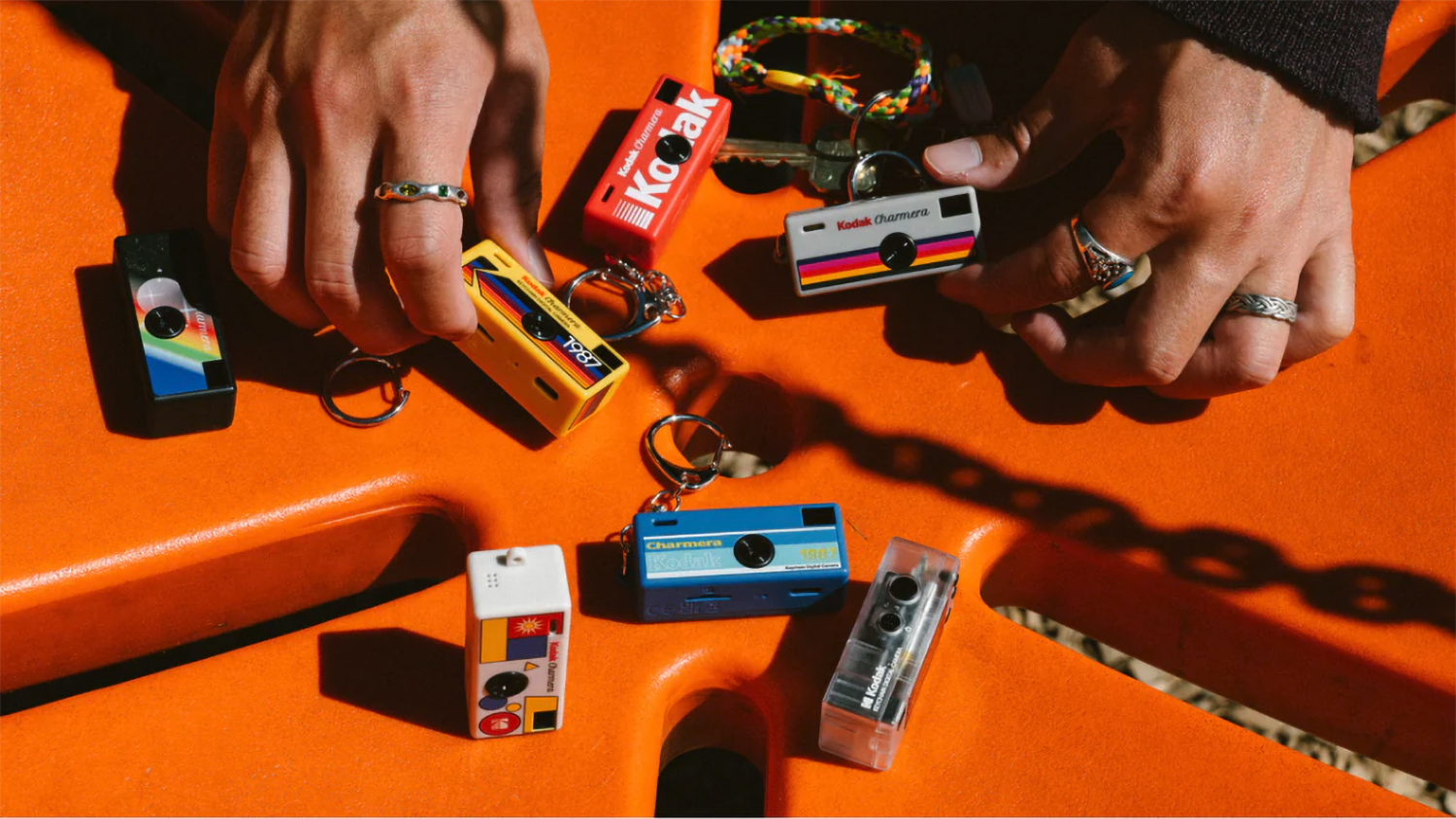 Kodak Charmera keyring camera in all six colorways, on a bright orange surface in sunlight