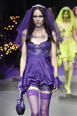 seorang model berjalan di runway mengenakan gaun ungu kusut dan kerudung