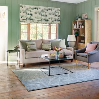 Living room with light green wall panelling, wooden floor, pale pink sofa and floral blinds