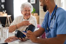 Happy healthcare worker or caregiver visiting senior woman indoors at home, measuring blood pressure. 