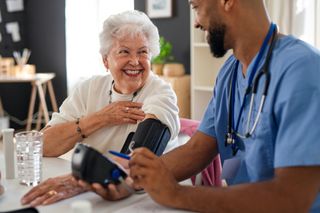 Happy healthcare worker or caregiver visiting senior woman indoors at home, measuring blood pressure.