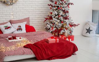 A bedroom decorated for Christmas with a white Christmas tree and red baubles, and red gingham bedding.