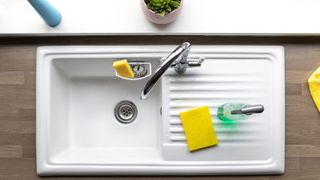 White ceramic sink shot from above, with silver faucet, yellow sponge and spray