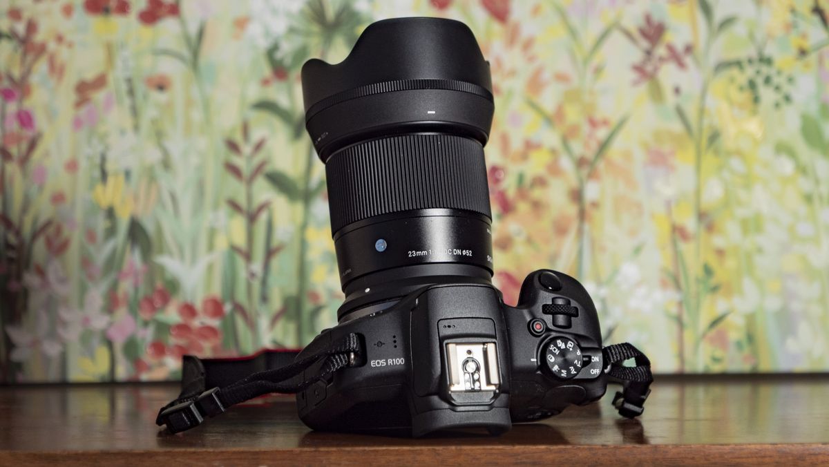 Sigma 23mm F1.4 DC DN Contemporary lens attached to a Canon EOS R100, on a wooden surface with floral backrop