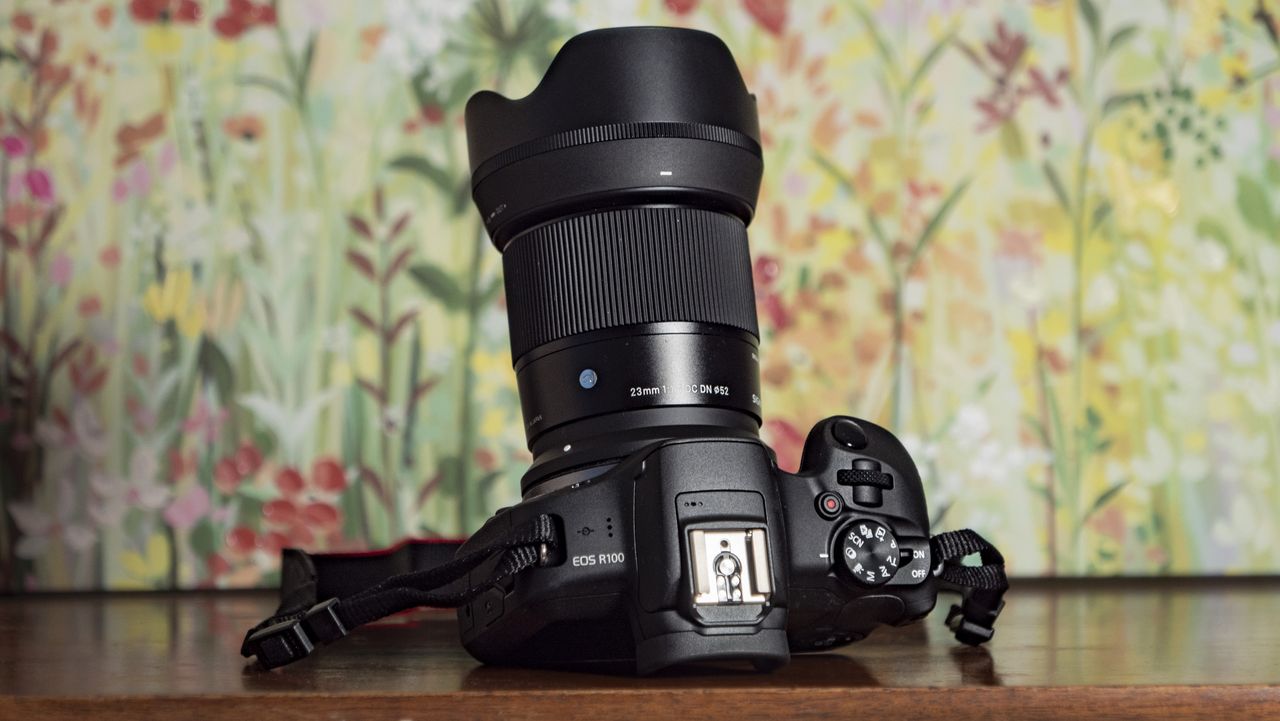 Sigma 23mm F1.4 DC DN Contemporary lens attached to a Canon EOS R100, on a wooden surface with floral backrop
