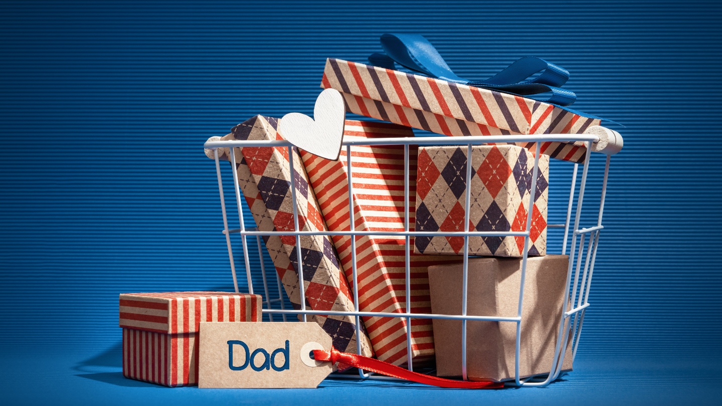 Blue background with a basket full of wrapped Father&#039;s Day gifts with a tag that says Dad on it