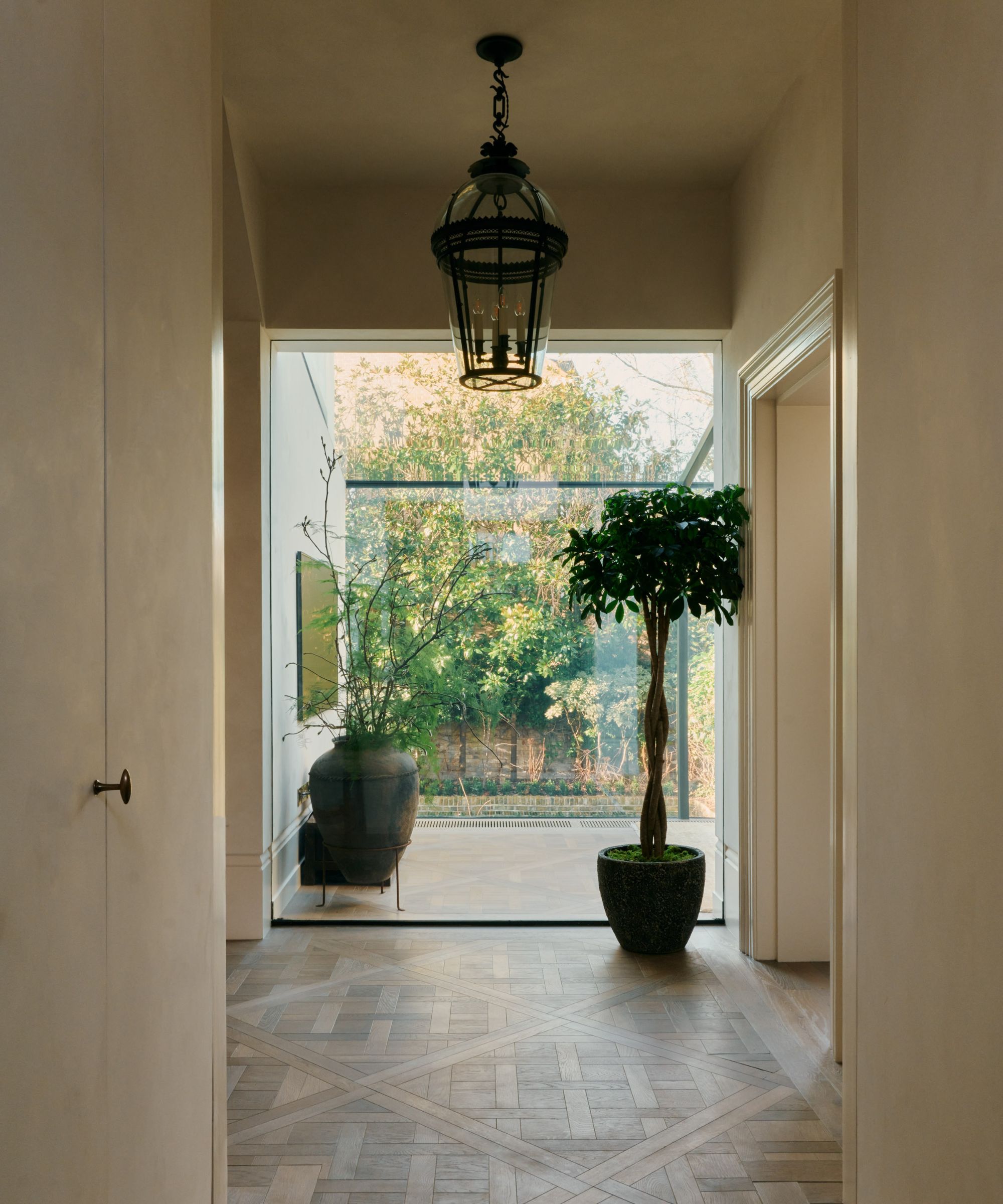 Large entryway with tiled floor, plant pot, floor to ceiling window with courtyard and greenery in background