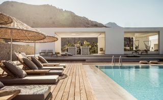 Hotel pool with umbrellas and loungers on a wooden deck.