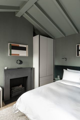 A loft bedroom painted sage green with a grey fireplace