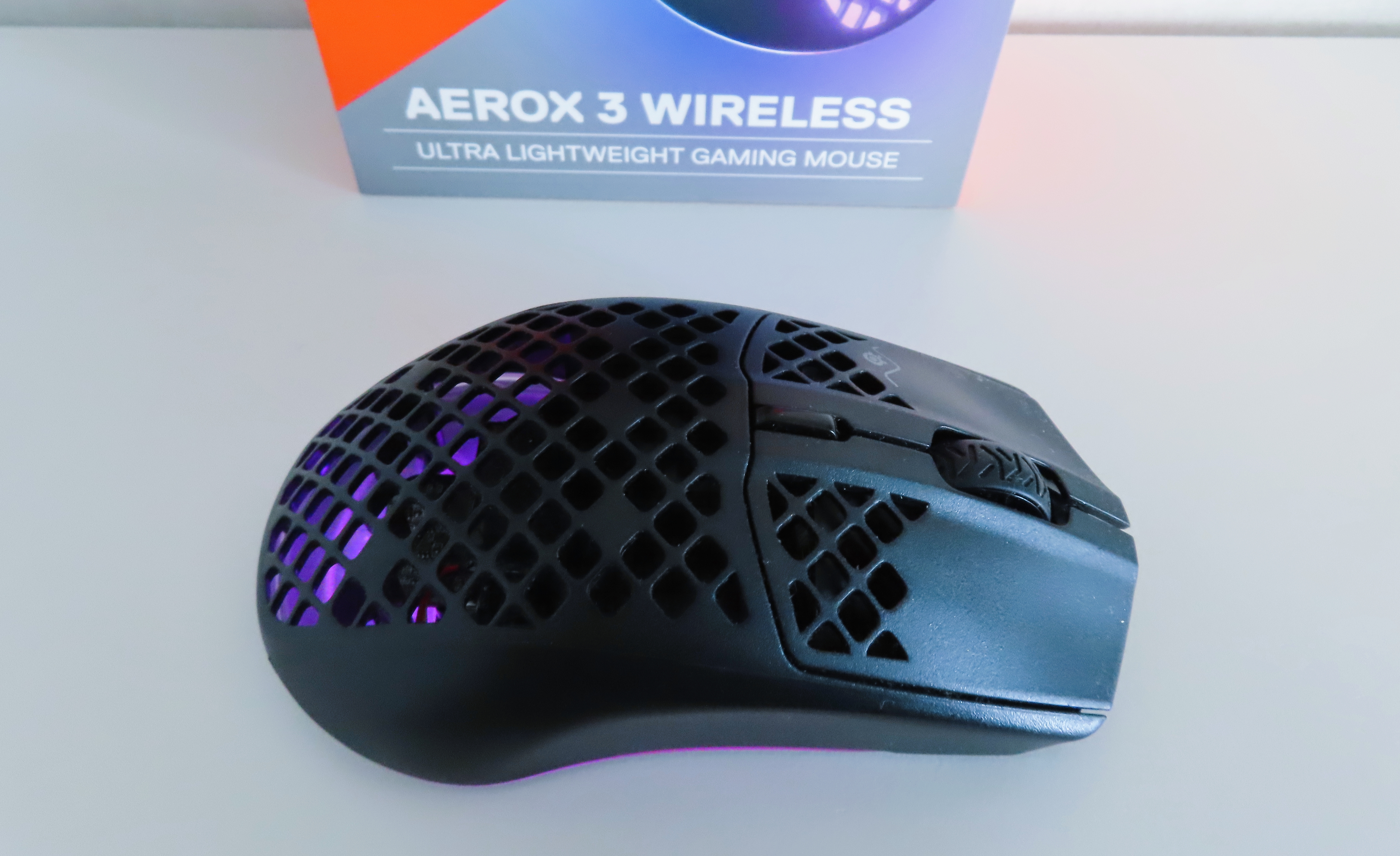 En svart SteelSeries Aerox 3 ligger på ett vitt bord med den tillhörande förpackningen bredvid.