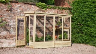 A wooden lean-to greenhouse set against a red brick garden wall