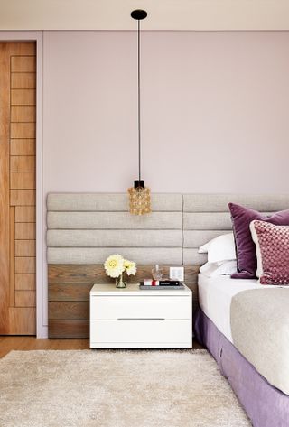 Bedroom with lavender wall and bed base, beige upholstered headboard and rug, and wood panelling