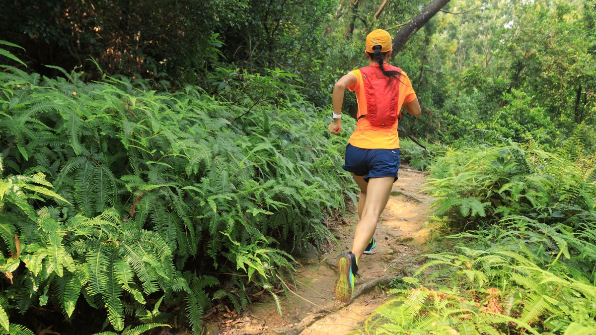 Woman with backpack running through woodland