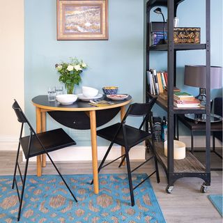 blue wall with black drop leaf table and chairs and shelving unit