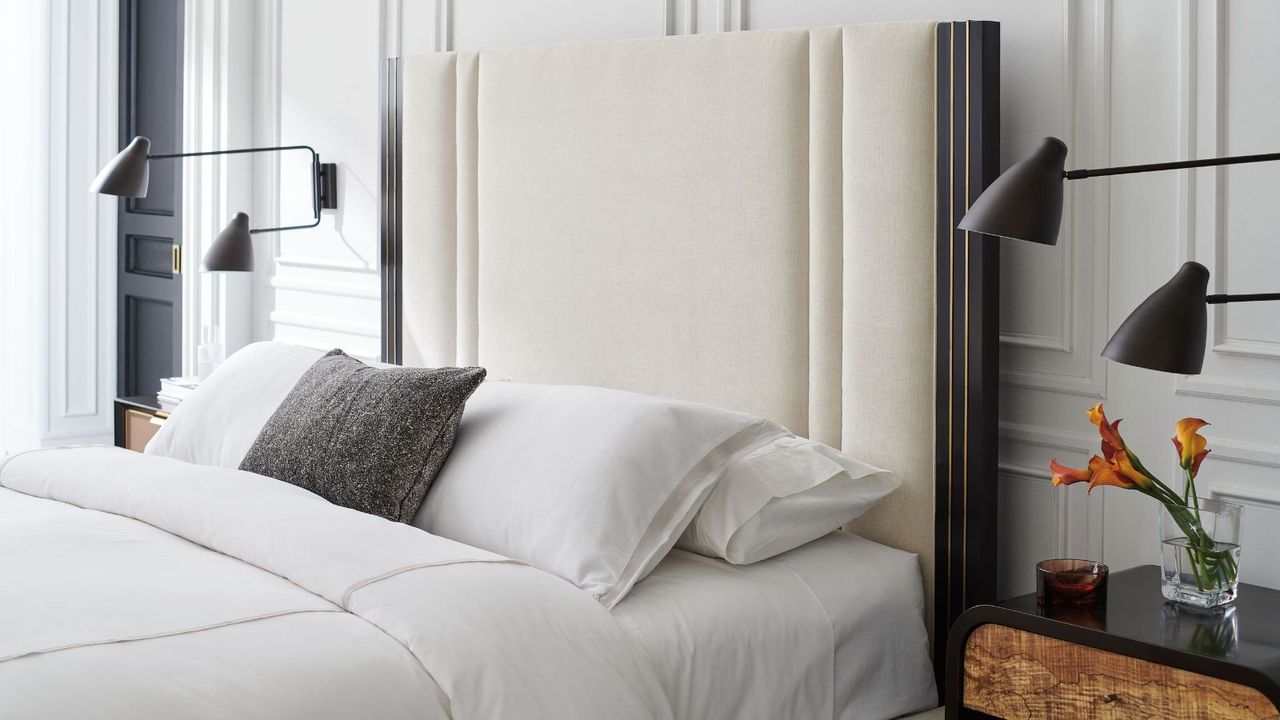 A bed with white padded headboard made with white bedding and a blue throw pillow