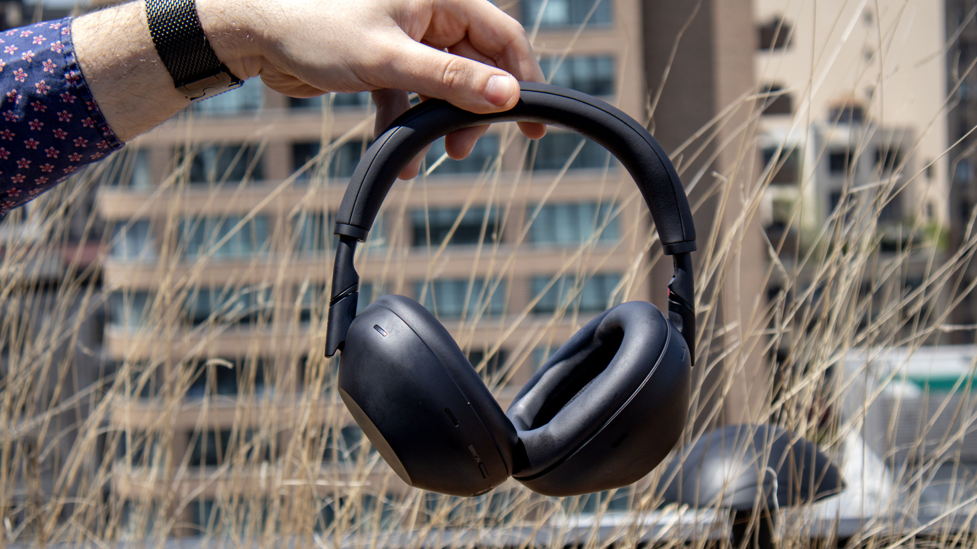 Black Sony WH-1000XM6 noise-cancelling headphones held outdoors in sunshine