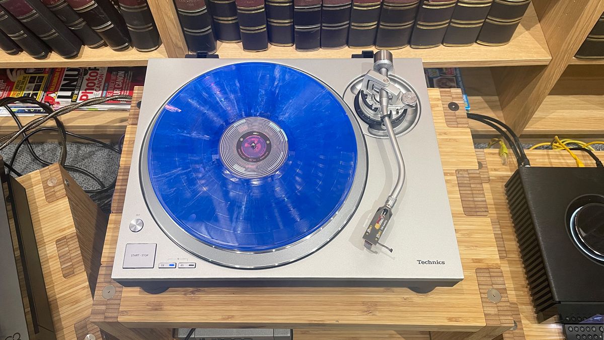 Technics SL-1300G turntable on wooden hi-fi rack in front of bookcase with blue vinyl record on platter