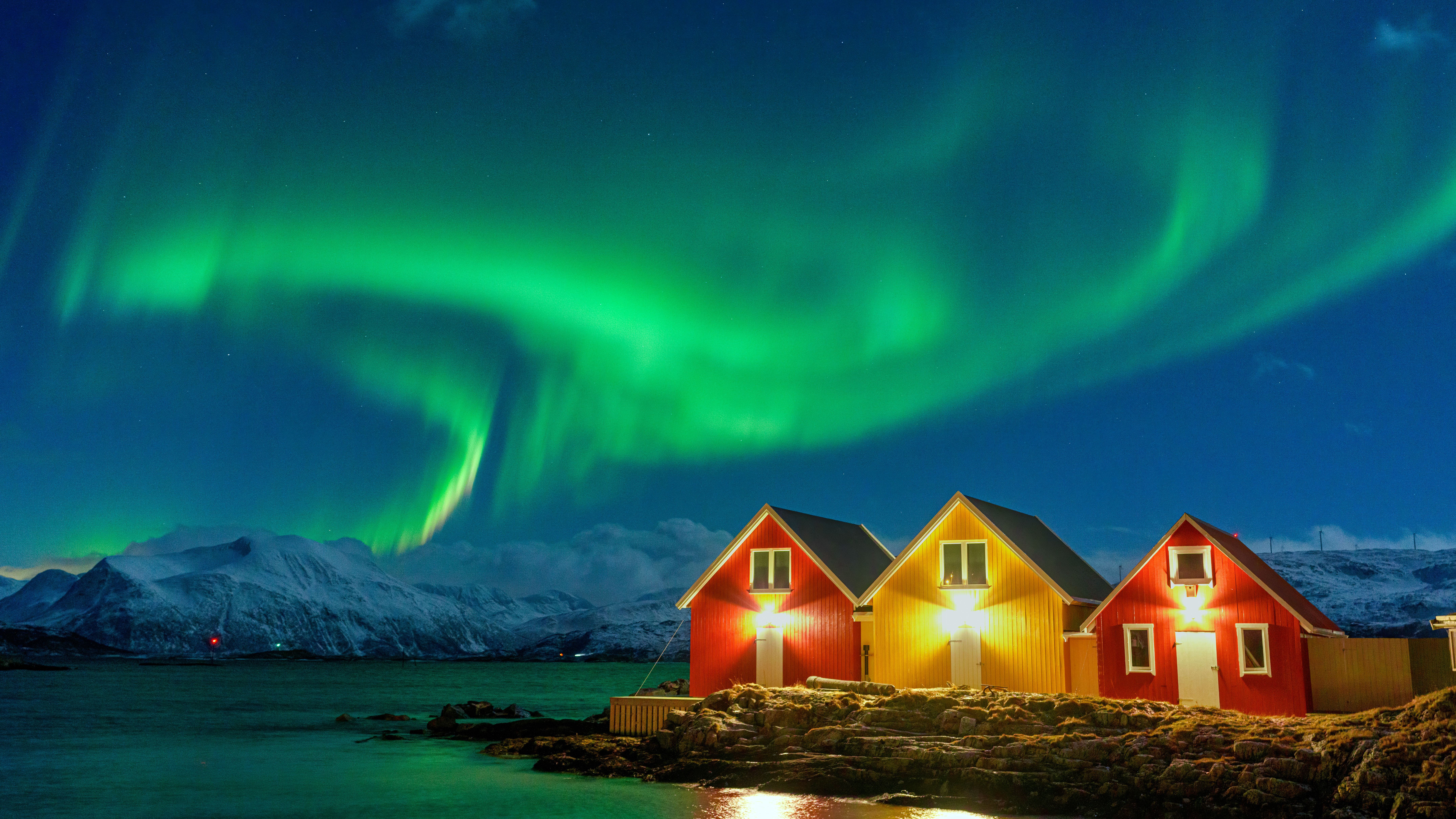 Aurora Borealis over snowcapped mountains and fishermen cabins by the sea, Sommaroy, Troms og Finnmark, Norway