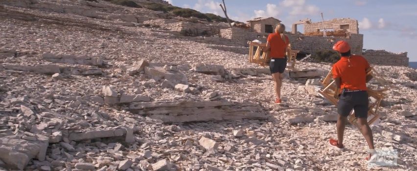 Bosun Malia and deck hand Mzi lug chairs and tables up a steep hill to prepare for a guest picnic in an abandoned film set.