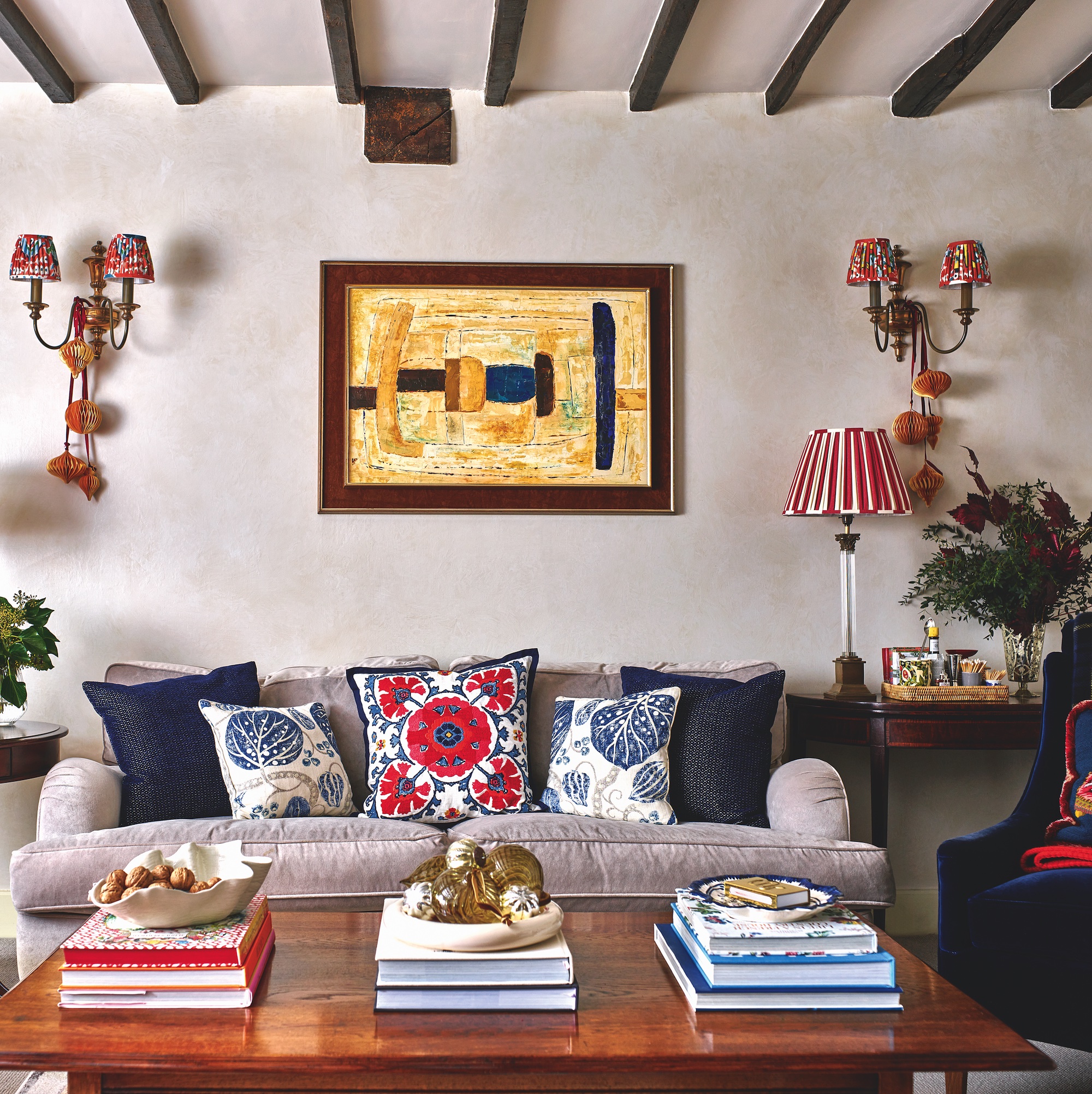 living room with sofa covered with cushions, wooden coffee table piled with books, and David Hunt wall lights