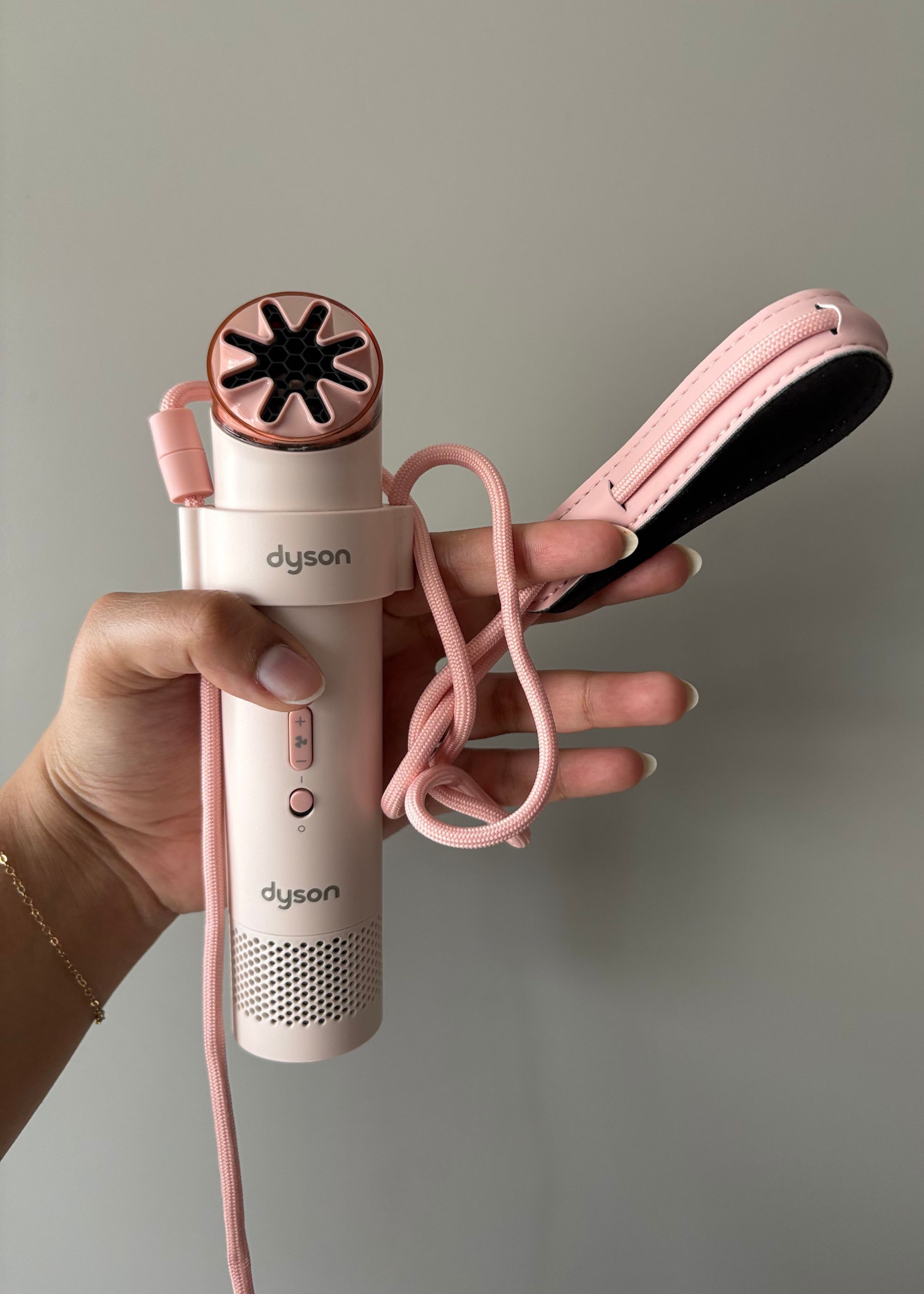 A hand holding the Dyson HushJet Mini Cool Fan and its strap