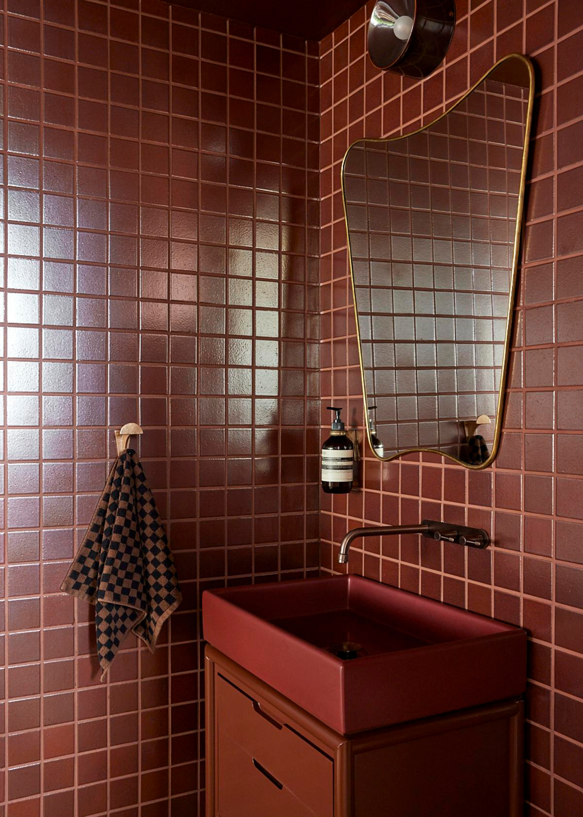 dark red tiled bathroom with a matching red sink and a gold mirror