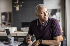Senior man using smartphone and looking out window at home