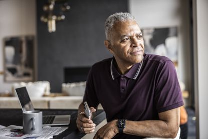 Senior man using smartphone and looking out window at home
