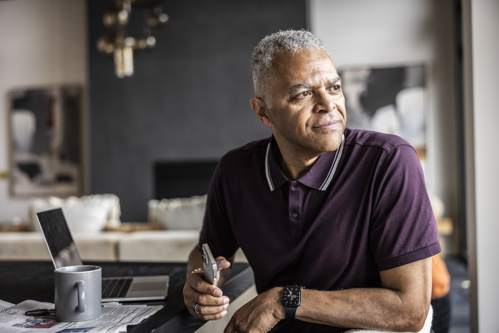 Senior man using smartphone and looking out window at home