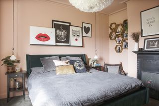Peach pink painted bedroom with dark velvet bed, grey bed sheets, black and red art on picture shelf