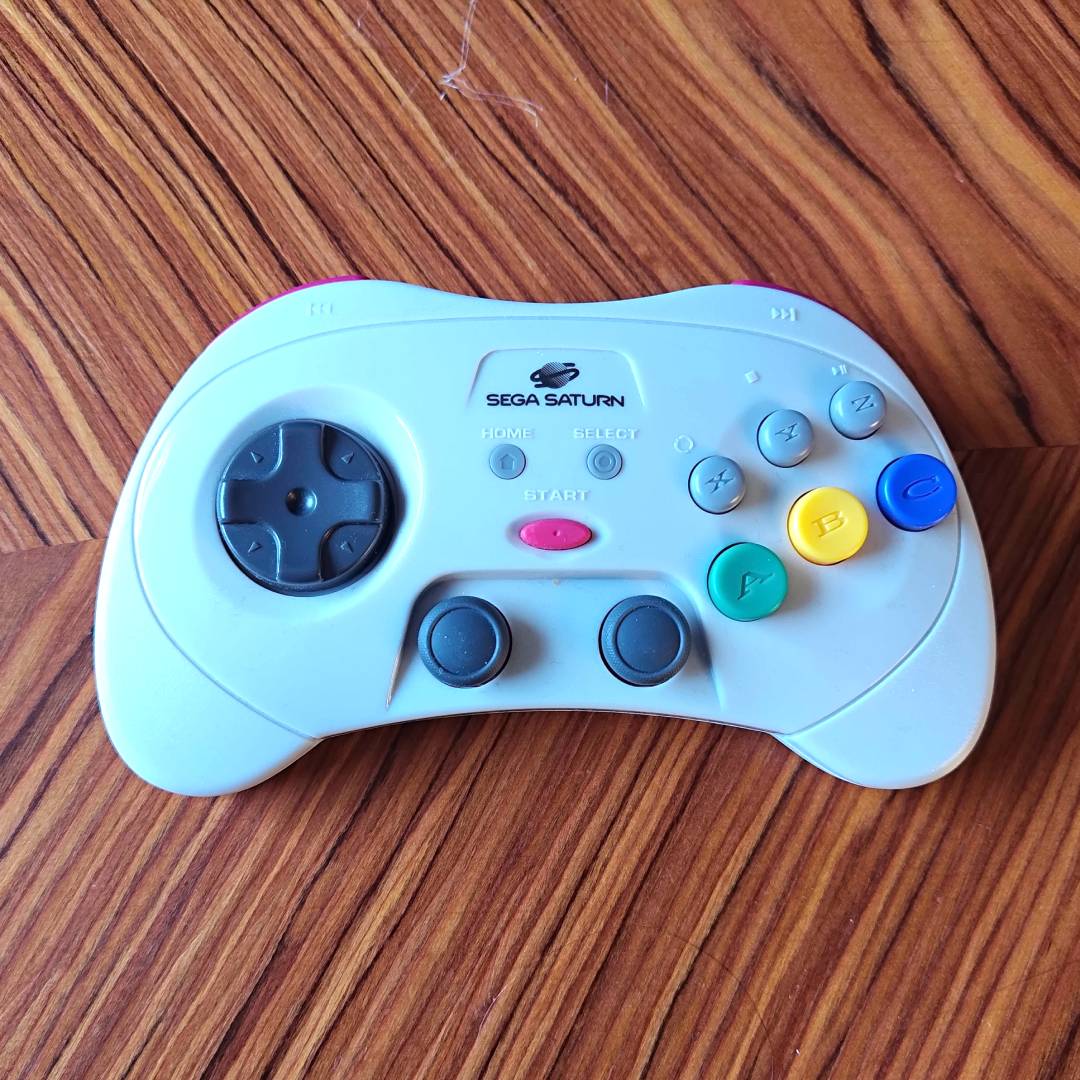 Retro-bit Sega Saturn Pro controller in white sitting on woodgrain table.
