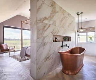 open plan bathroom concept with dividing wall with copper freestanding bath on one side, built in storage and bed on other side