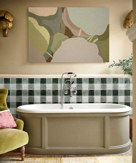 A warm bathroom with green and white gingham tiles on the lower half of the wall behind a freestanding bath clad in soft olive