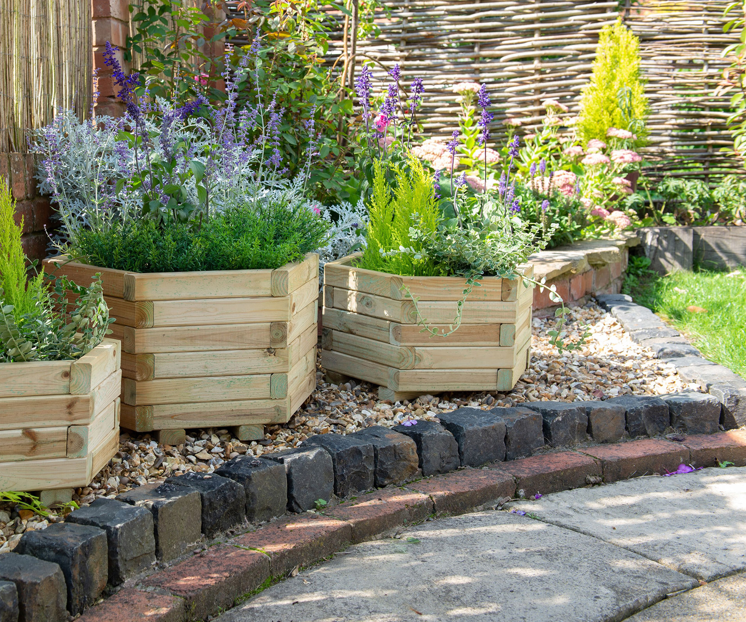 Timber garden planters in a gravel garden border edged with brick and setts