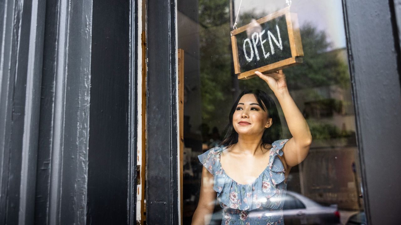 Female small business owner turning around &quot;open&quot; sign on the front door of her store