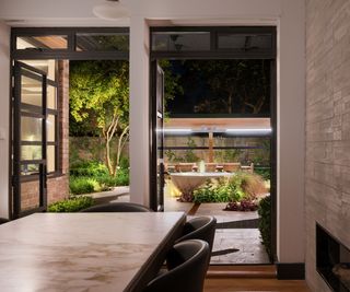 A view through a kitchen out the back doors looking at a well lit garden