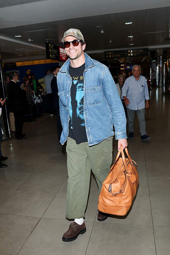 Paul Anthony Kelly is seen arriving on June 15, 2026 in Florence, Italy wearing a denim shacket, band tee and green trousers