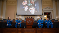 Four Artemis 2 astronauts sit on Capitol Hill and look up at an image from their flight. 
