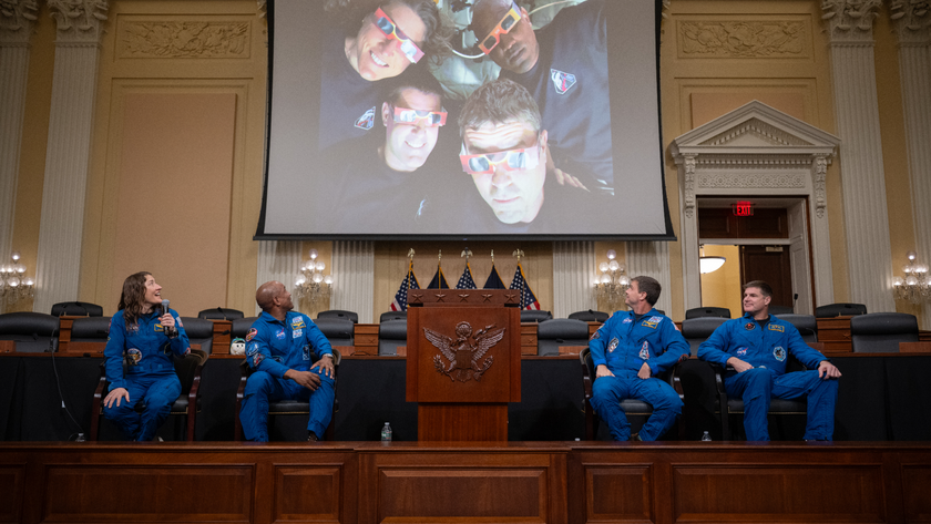 Four Artemis 2 astronauts sit on Capitol Hill and look up at an image from their flight. 