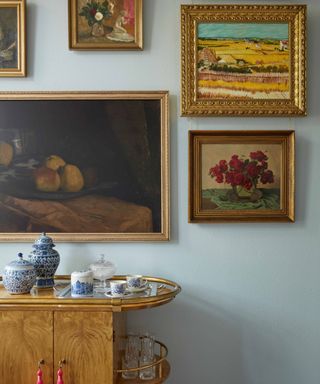 A light blue wall behind a collage of vintage gold frames and a small bar