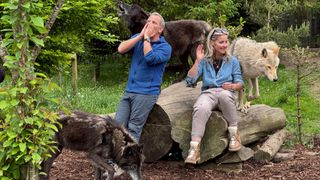 Robson Green and Helen Skelton sitting on a log with wolves on Robson Green's Weekend Escapes