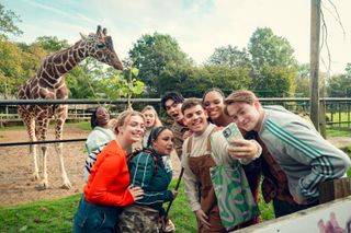 The cast of 'Heartstopper' takes a selfie with a giraffe, in 'Heartstopper' season 3.